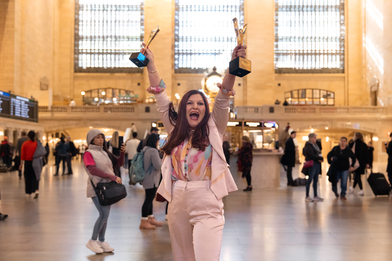 Annie Gibbins at Grand Central Station, New York, holding her two Stevie Award statuettes aloft after winning Grand Stevie for Women in Business 2023